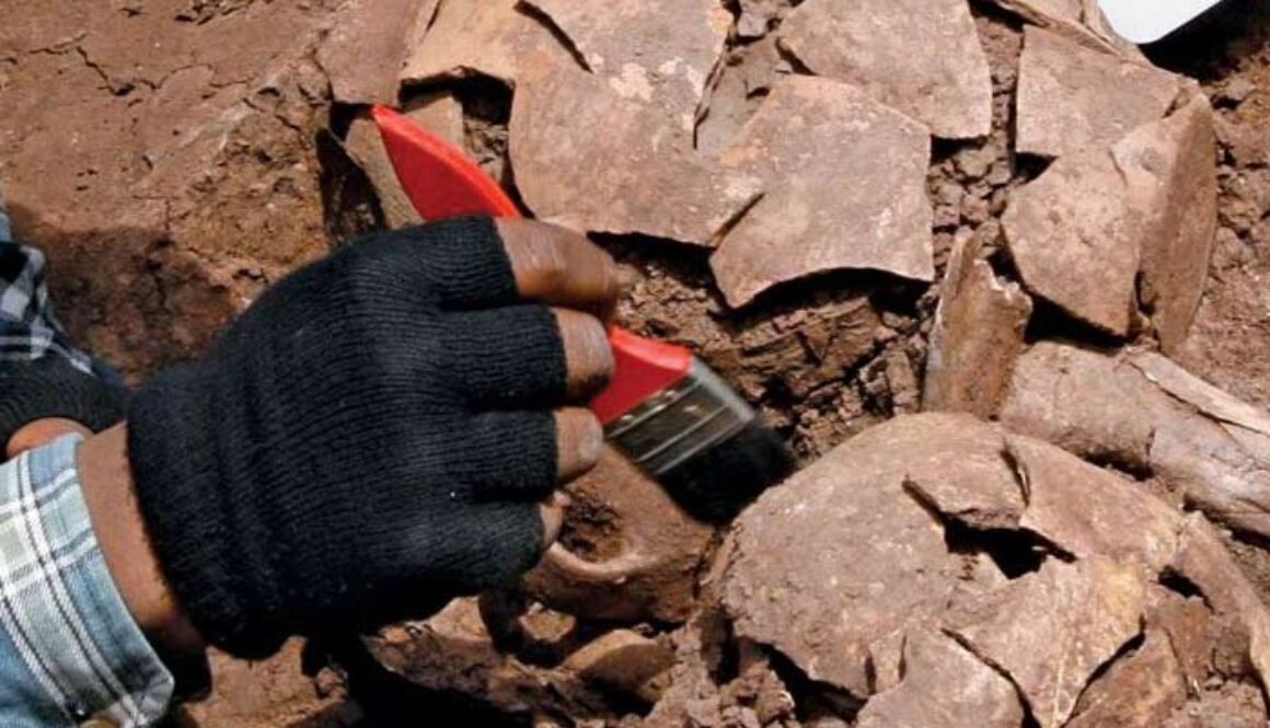 hand holding brush excavating old pottery