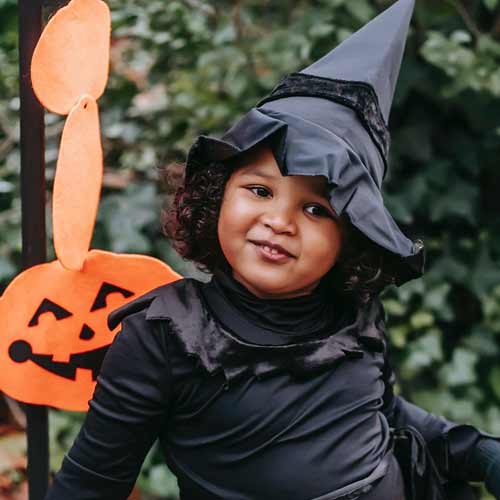 young girl in witches costume with pumpkin in background